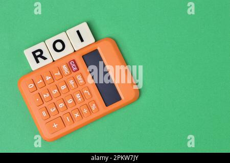 Calculatrice et lettres carrées avec texte ROI signifie Return on Investment sur fond vert. Banque D'Images