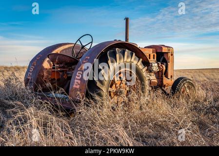 Coderre, SK- 9 avril 2020 : coucher de soleil sur un tracteur de case ancien abandonné dans la haute herbe des Prairies en Saskatchewan Banque D'Images