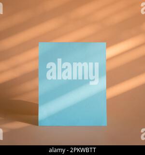 Feuille de papier vierge bleue avec fond beige, lumière du soleil et ombres. Modèle de marque commerciale. Banque D'Images