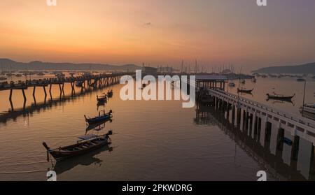 Vue aérienne des bateaux de pêche sur la plage à l'embarcadère de Chalong au lever du soleil. Lever de soleil avec des rayons de lumière jaune doux et d'autres effets atmosphériques. coloré Banque D'Images