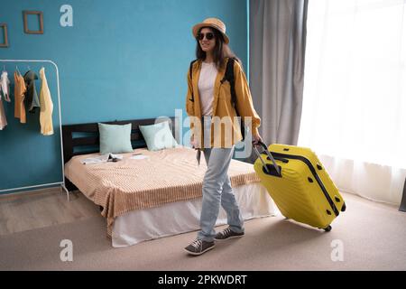 Une dame joyeuse est excitée de quitter la maison pour un voyage. Femme tirant une valise sur le point de sortir de sa maison pour voyager. Copier l'espace Banque D'Images