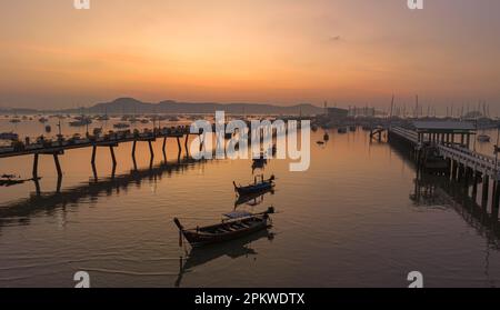 Vue aérienne des bateaux de pêche sur la plage à l'embarcadère de Chalong au lever du soleil. Lever de soleil avec des rayons de lumière jaune doux et d'autres effets atmosphériques. coloré Banque D'Images