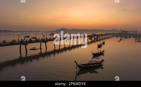 Vue aérienne des bateaux de pêche sur la plage à l'embarcadère de Chalong au lever du soleil. Lever de soleil avec des rayons de lumière jaune doux et d'autres effets atmosphériques. coloré Banque D'Images