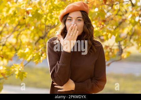 Belle femme choquée marchant à l'extérieur en automne, regardant la caméra couvrant sa bouche avec la main. Copier l'espace Banque D'Images