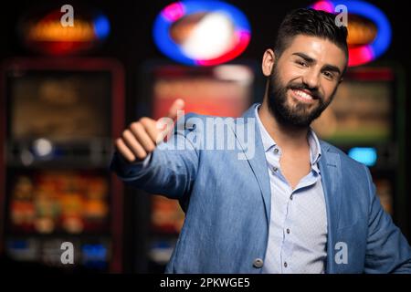 Portrait d'un jeune homme arabe beau et bien habillé jouant dans le Casino et montrant Thumbs Up Banque D'Images