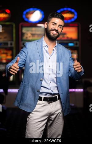 Portrait d'un jeune homme arabe beau et bien habillé jouant dans le Casino et montrant Thumbs Up Banque D'Images