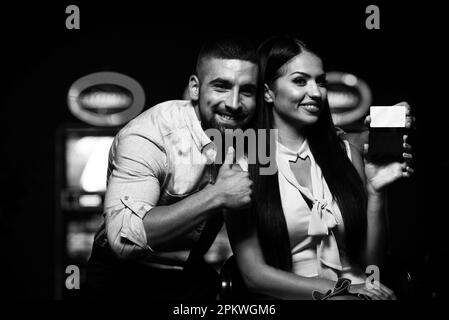 Portrait d'un jeune couple beau et bien habillé jouant au Casino et célébrez la tenue de la carte VIP et l'homme montrant des Thumbs Up Banque D'Images