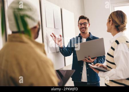 Équipe commerciale créative ayant une discussion en se tenant à côté de quelques panneaux d'affichage dans un bureau. Groupe de divers hommes d'affaires ayant une réunion à Banque D'Images