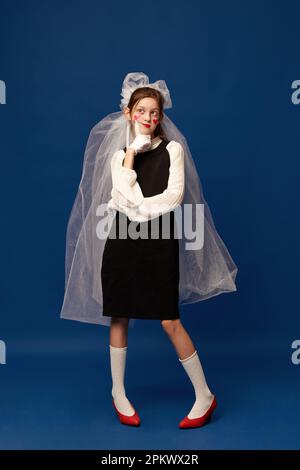 Une jeune fille pensive portant le voile de mariée pensant à se marier sur fond de studio bleu Banque D'Images