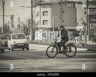 Bucarest, Roumanie - Mars 2023: Homme traversant la rue sur un vélo avec beaucoup de voitures en arrière-plan. Circulation dans la rue à Bucarest. Banque D'Images