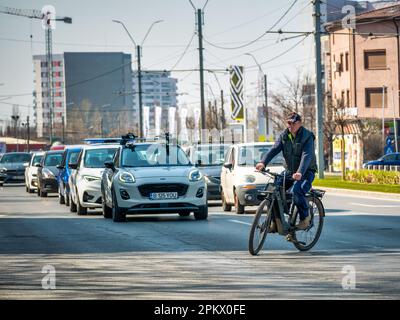 Bucarest, Roumanie - Mars 2023: Homme traversant la rue sur un vélo avec beaucoup de voitures en arrière-plan. Circulation dans la rue à Bucarest. Banque D'Images