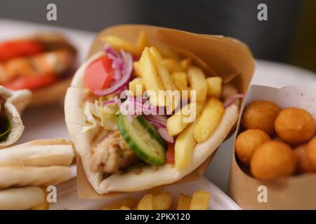 Délicieux sandwich gyros grec avec frites et filet de porc servi pour un repas à emporter dans un restaurant de restauration rapide. Collation de viande enveloppée préparée pour le déjeuner dans un Banque D'Images