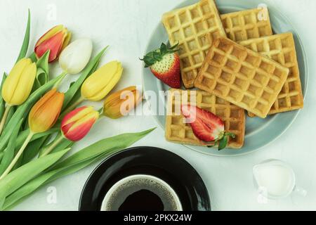 Tulipes fraîches et gaufres de fruits belges, vue de dessus. Petit déjeuner savoureux. Petit déjeuner pour un être cher. Gaufres faites maison sur une assiette. Arrière-plan avec espace de copie Banque D'Images