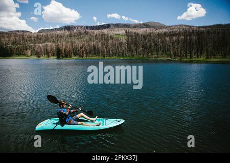 Un jeune garçon fait du kayak sur une belle eau bleue avec des montagnes et du ciel Banque D'Images