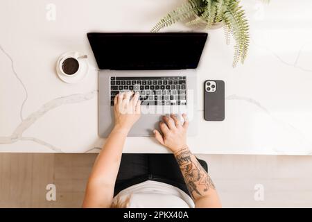Tatoués armes dactylographiant sur un ordinateur avec un expresso et un téléphone Banque D'Images
