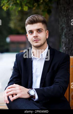 un homme en costume est assis dans le parc sur un banc avant une réunion d'affaires Banque D'Images