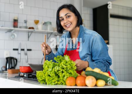 Bonne femme hispanique préparant des plats végétariens ou végétaliens avec des tomates et des pommes de terre et de la salade Banque D'Images