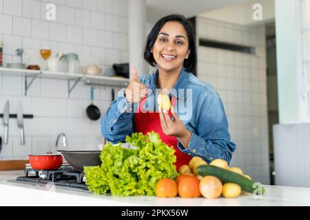 Jolie femme hispanique préparant des aliments végétariens ou végétaliens avec des tomates et des pommes de terre et de la salade Banque D'Images