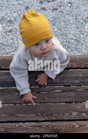 Tout-petit en chapeau jaune se tient sur un sentier de galets lumineux près d'un banc brun Banque D'Images