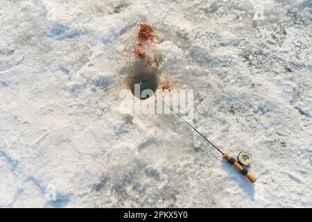 La canne à pêche repose sur la neige à côté du trou Banque D'Images