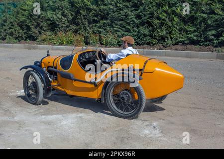 Jeune homme avec Austin 7 voiture d'époque conduite sur une route de terre. Banque D'Images