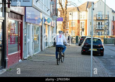 Un cycliste âgé qui fait du vélo sur la chaussée avec des voitures garées sur le trottoir dans une rue de banlieue, Shepperton Surrey, Angleterre, Royaume-Uni Banque D'Images