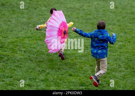 Preston Lancashire. Météo Royaume-Uni. 10 avril 2023. Joyeuse jeune fille en haut jaune avec un parapluie pétale rose au lundi de Pâques traditionnel Egg-Rolling dans Avenuam Park, une tradition datant de 1867. Les enfants roulent leurs œufs de rythme dans les collines et voient qui pourrait obtenir le leur le plus loin sans qu'il se casse. Crédit MediaWorldmages/AlamyLiveNews Banque D'Images