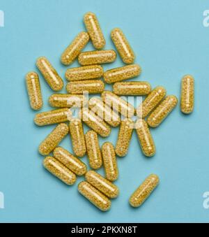 Capsules médicales transparentes avec granules jaunes à l'intérieur sur fond bleu, comprimés pour le traitement, vitamines Banque D'Images