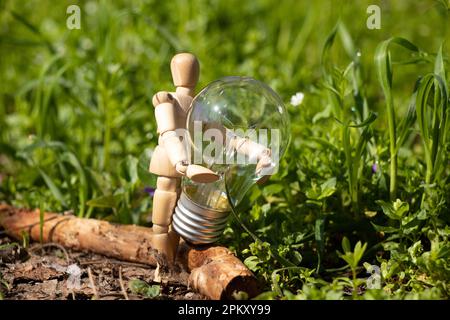 Un petit homme en bois tient une ampoule incandescente sur l'herbe dans les parcs en Ukraine , électricité Banque D'Images