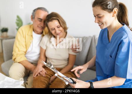 Infirmière à domicile en visite à un couple de personnes âgées à la maison, assis sur un canapé et parlant, discutant des résultats des examens médicaux Banque D'Images