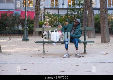 Un homme plus âgé profite d'un moment calme sur un banc de jardin, en prenant une pause des rues animées de la ville tout en appréciant une fumée. Banque D'Images