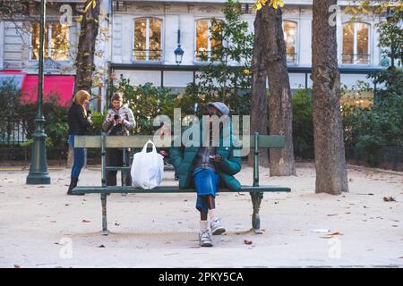 Un homme plus âgé profite d'un moment calme sur un banc de jardin, en prenant une pause des rues animées de la ville tout en appréciant une fumée. Banque D'Images