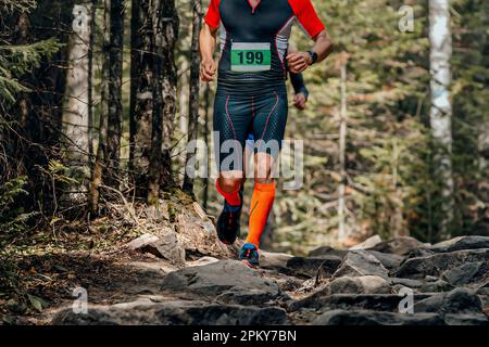 coureur masculin en chaussettes de compression course de forêt au-dessus de pierres, course de marathon d'été Banque D'Images