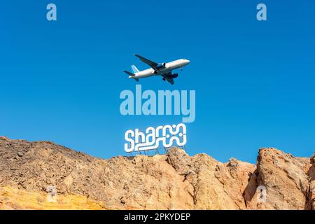 Panneau SHARM sur les rochers sur fond de ciel avec avion. Destination du voyage. Banque D'Images