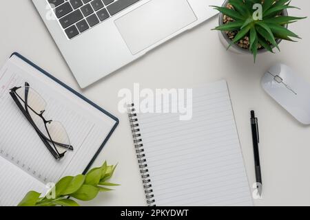 Espace de travail avec bloc-notes vierge, ordinateur portable, fournitures de bureau, feuille verte et lunettes sur fond blanc. Bureau avec table et vue sur le dessus. Banque D'Images
