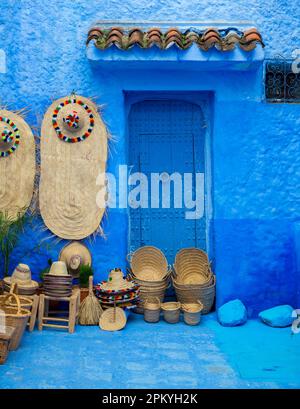 Vente de chapeaux et paniers en paille traditionnellement faits, devant une porte bleue, Maroc Banque D'Images