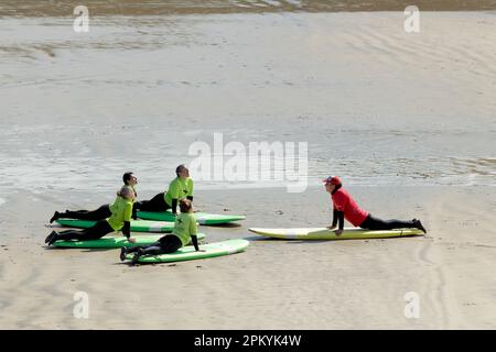 Cornwall: Un groupe d'élèves de sexe féminin qui enseigne certaines manoeuvres de base à une école de surf par un instructeur. Les élèves sont allongés sur des planches de surf Banque D'Images