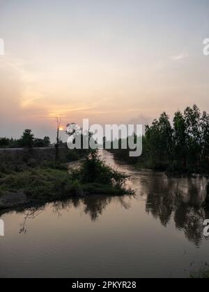 Le ruisseau qui coule dans le canal pour l'irrigation qui est le long de la route à côté des rizières dans la soirée, vue de face avec l'espace copie. Banque D'Images