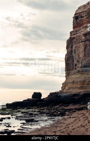 Vue pittoresque des falaises rocheuses rugueuses avec surface inégale près de la mer sur la plage contre ciel nuageux en soirée Banque D'Images