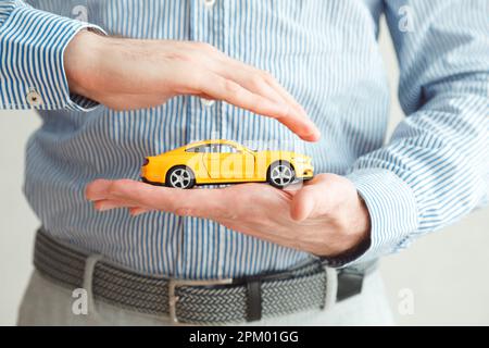 Agent d'assurance homme tenant une voiture miniature, couvrant avec des palmiers, car Safe concept. Banque D'Images