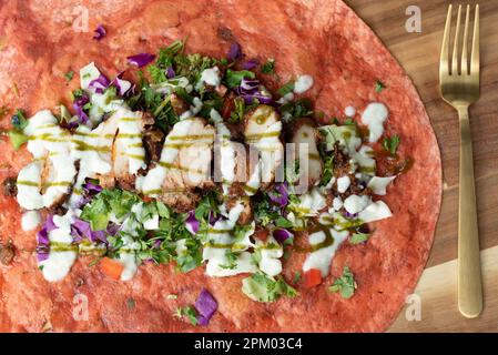 Un gros plan d'un plat mexicain fraîchement préparé à base de tortilla et recouvert de poulet grillé, de légumes et d'une sauce spéciale Banque D'Images