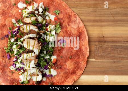 Un gros plan d'un plat mexicain fraîchement préparé à base de tortilla et recouvert de poulet grillé, de légumes et d'une sauce spéciale Banque D'Images