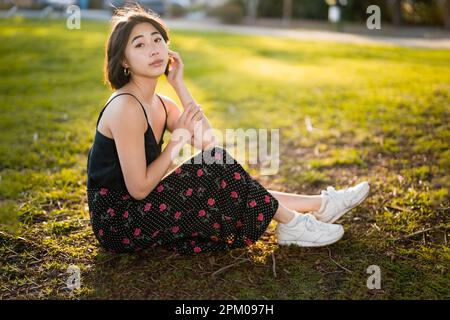 Jeune femme asiatique assise sur l'herbe dans un parc Palo Alto | Backlit | Moody | tons chauds Banque D'Images