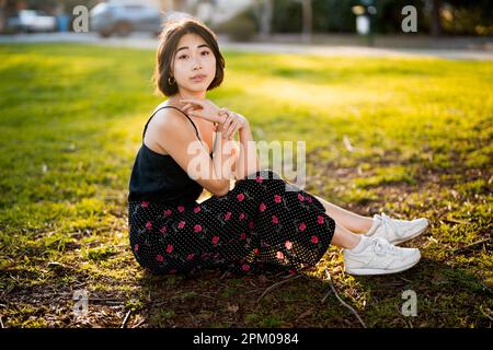 Jeune femme asiatique assise sur l'herbe dans un parc Palo Alto | Backlit | Moody | tons chauds Banque D'Images