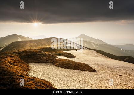 Vue sur les collines herbeuses avec des chaussettes orange et des montagnes enneigées en arrière-plan. Scène de printemps spectaculaire. Photographie de paysage Banque D'Images