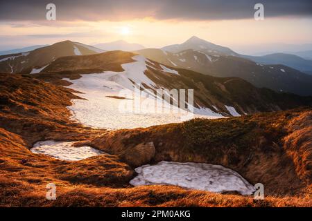 Vue sur les collines herbeuses avec des chaussettes orange et des montagnes enneigées en arrière-plan. Scène de printemps spectaculaire. Photographie de paysage Banque D'Images