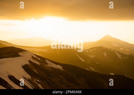 Vue sur les collines herbeuses avec des chaussettes orange et des montagnes enneigées en arrière-plan. Scène de printemps spectaculaire. Photographie de paysage Banque D'Images