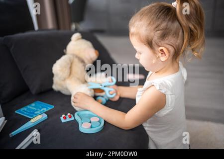 Petite fille jouant docteur avec des jouets et ours en peluche sur le canapé dans la salle de séjour à la maison Banque D'Images