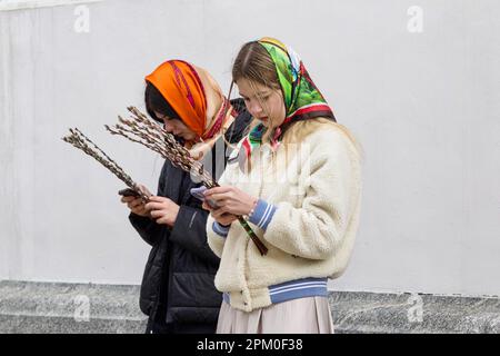 KIEV, UKRAINE - le 9 AVRIL 2023 - les jeunes femmes parcourent leur téléphone alors qu'elles tiennent des branches de saule pendant la liturgie divine à l'Église de Sain Banque D'Images