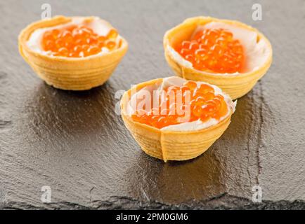 Tartelettes remplies de caviar de saumon rouge sur fond de pierre noire Banque D'Images